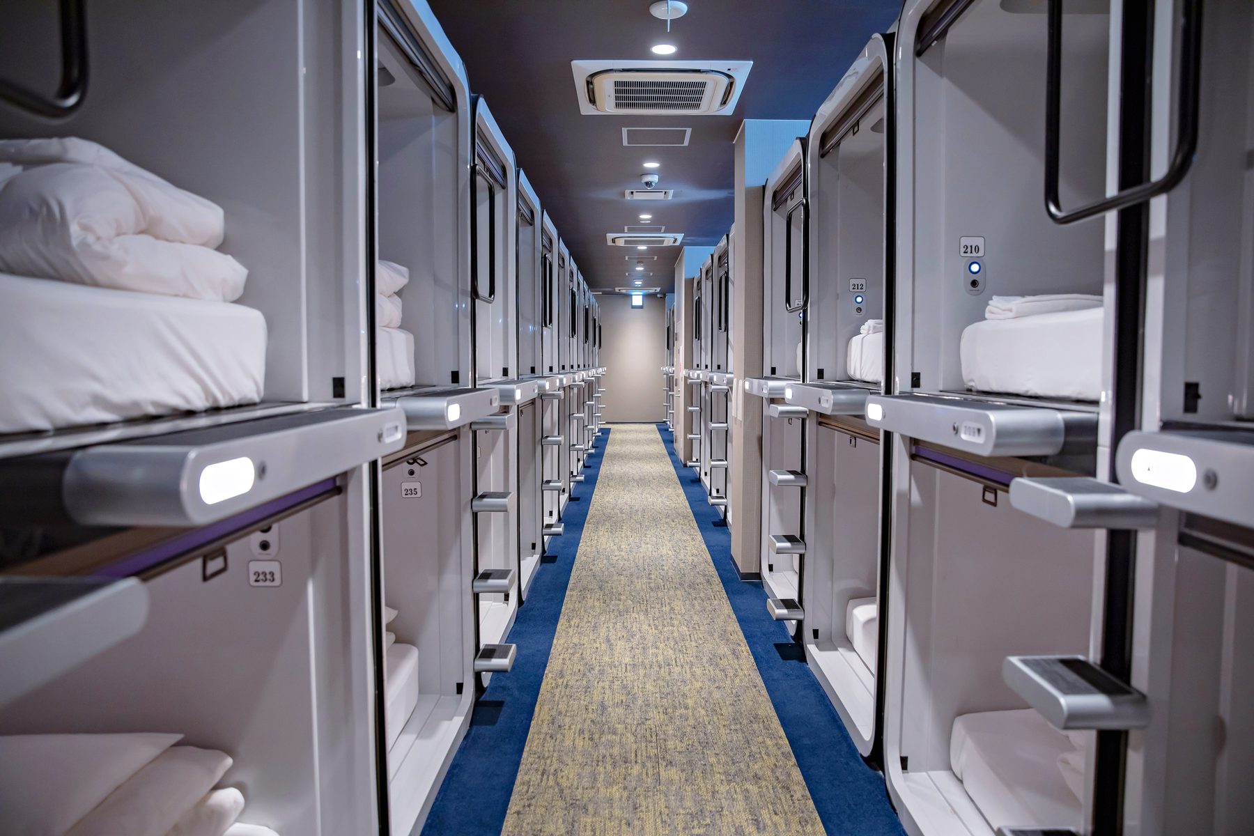 A corridor of white sleeping capsules with folded linen and reading lamps.