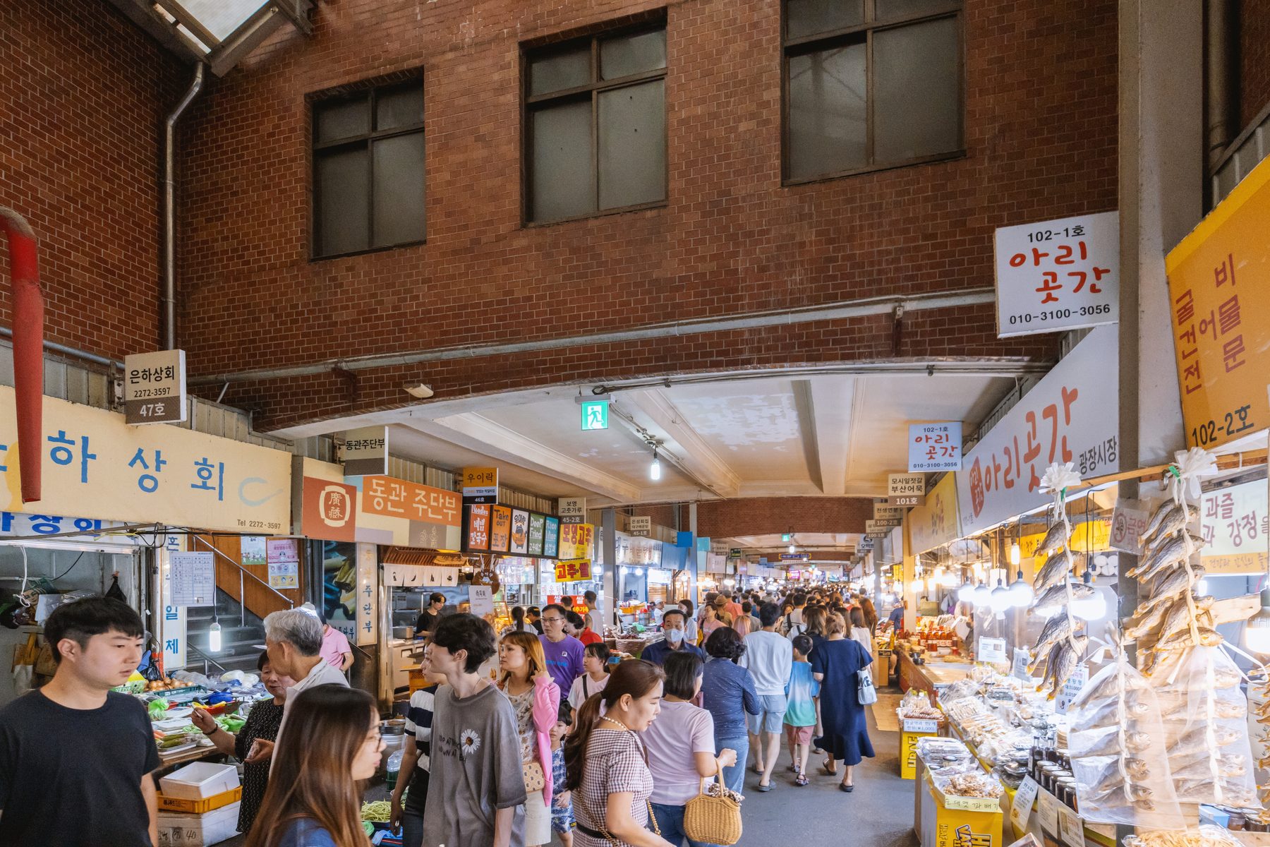 A crowded covered aisle at Gwangjang Market, with stalls and Korean shop signs on either side.