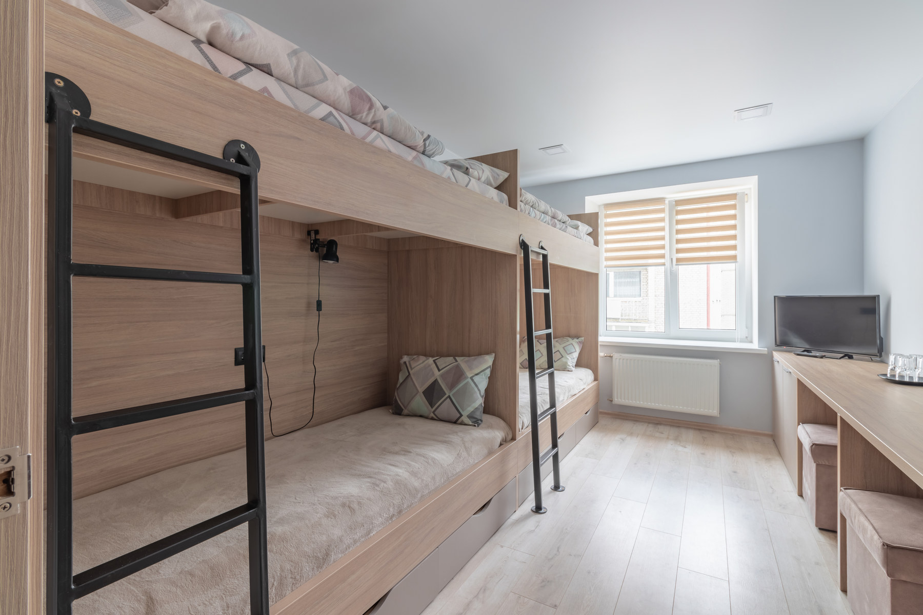 A narrow room lined with built-in wooden bunk berths, each with a small reading lamp, beside a window with slatted blinds.