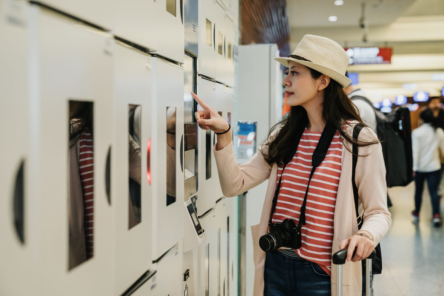 A traveller with a suitcase choosing a luggage locker on a touchscreen.
